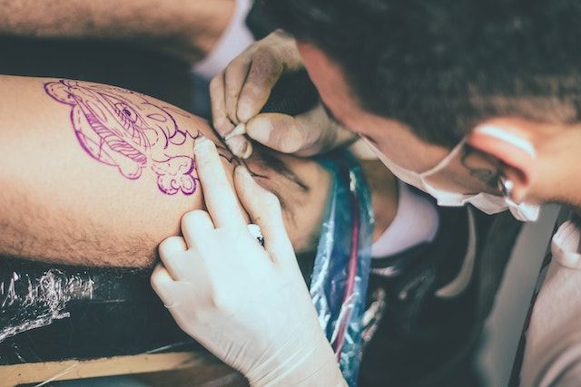 Tattooist drawing tattoo on client.