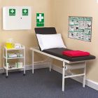 first aid room including posters, first aid cabinet, patient bed, bin and a white trolley with 3 shelves featuring gloves, dressings, hazardous waste bin, wipes and a tray